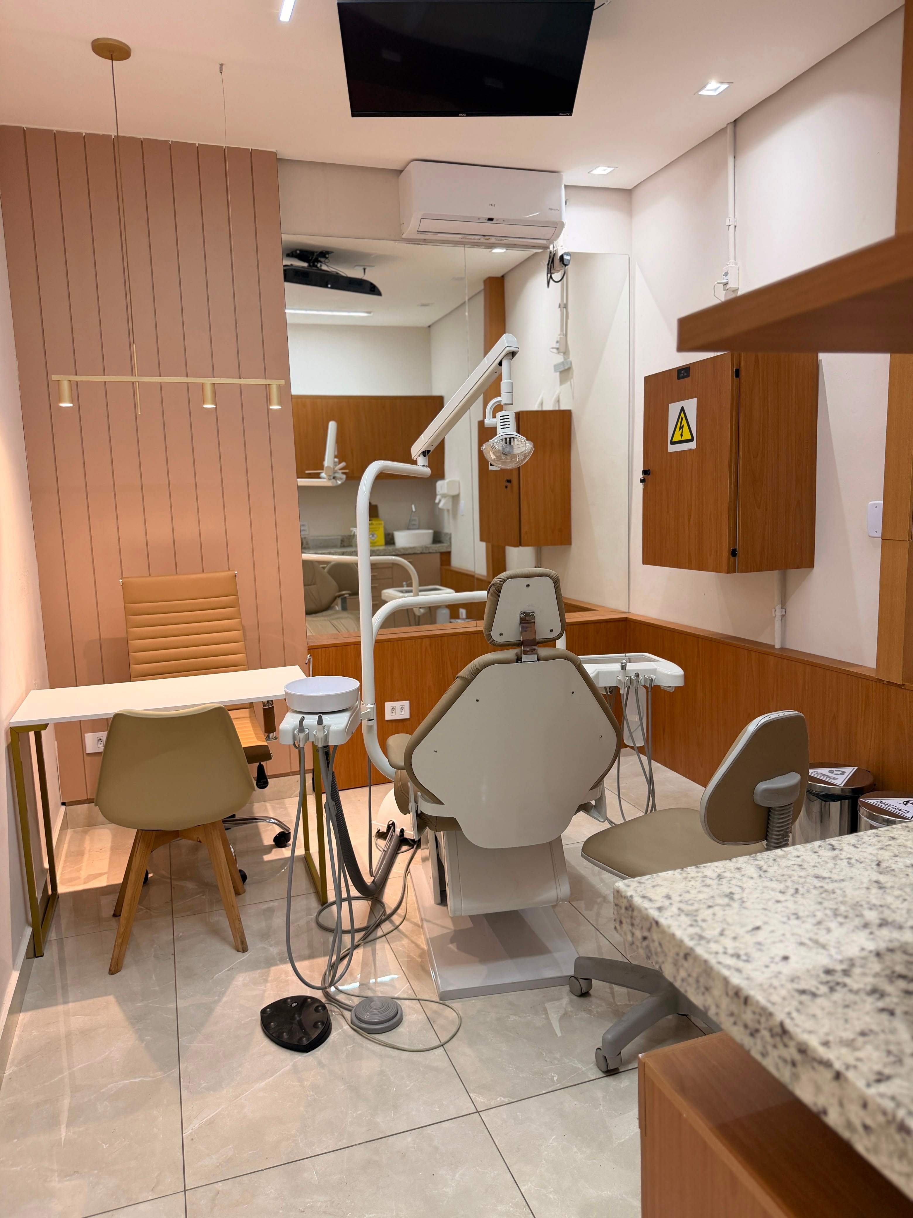 Consultório da Essence com cadeira odontológica, mocho e espelho refletindo outro ambiente de atendimento