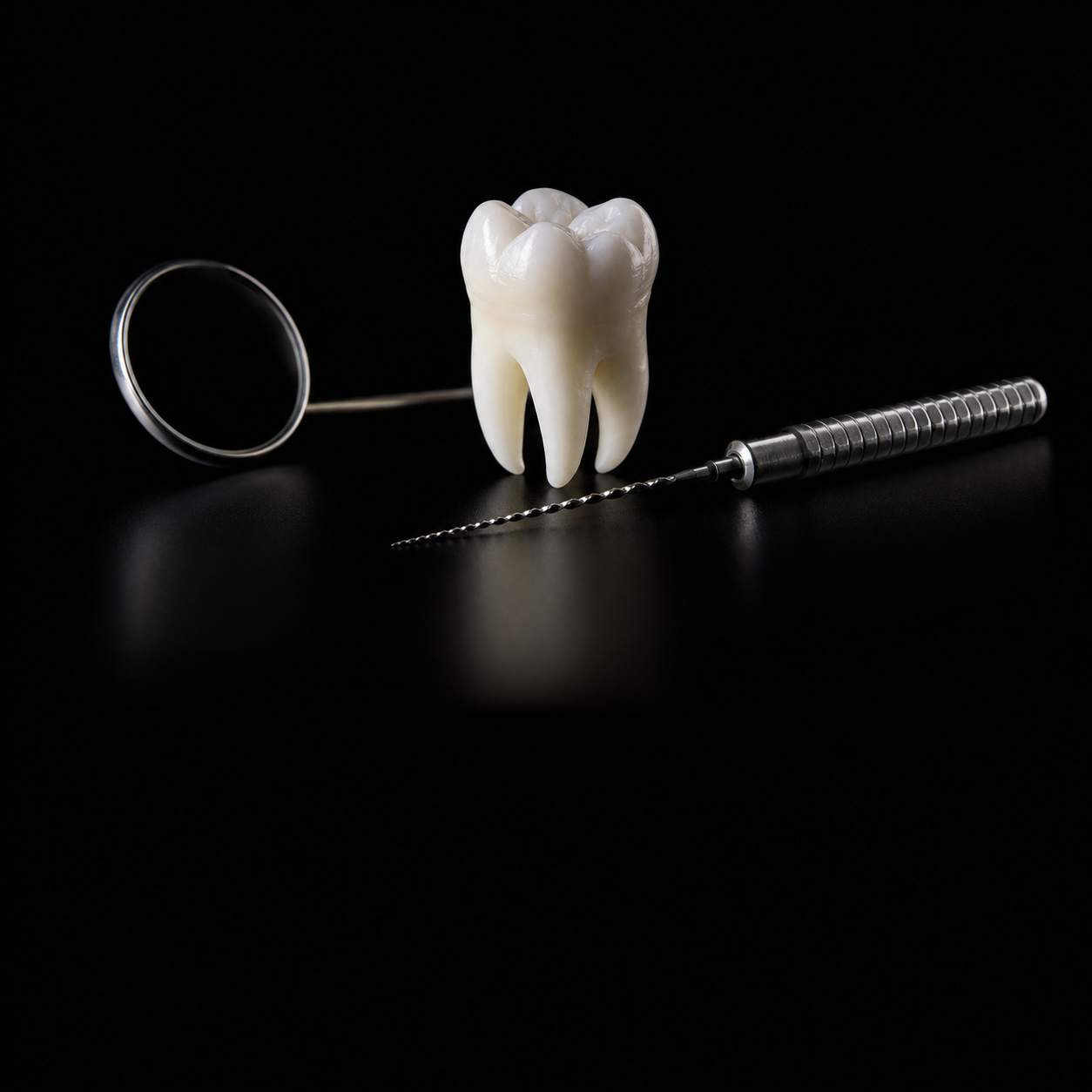 Espelho clínico, um dente e uma lima endodôntica sobre fundo preto